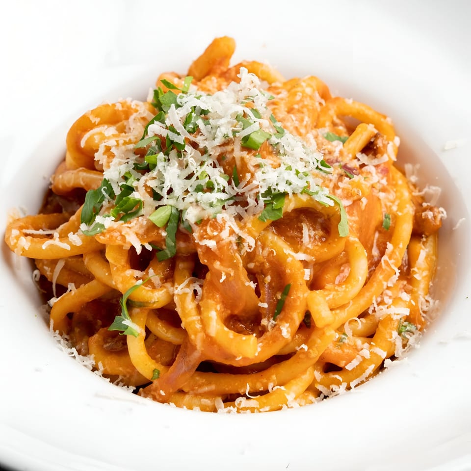 A white bowl filled with Italian pasta in a red sauce, topped with grated cheese and herbs.