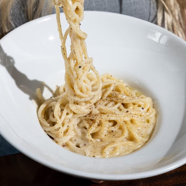 Creamy Italian spaghetti with black pepper being twirled on a fork from a white bowl.