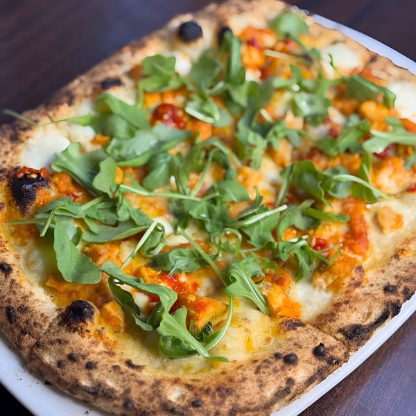 A square Italian pizza from Black Oak on Fifth, topped with fresh arugula, cheese, and tomato sauce.