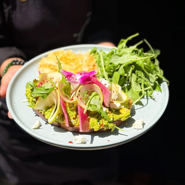 Avocado toast with radish, pear, feta, and arugula, served with hash browns on a plate.