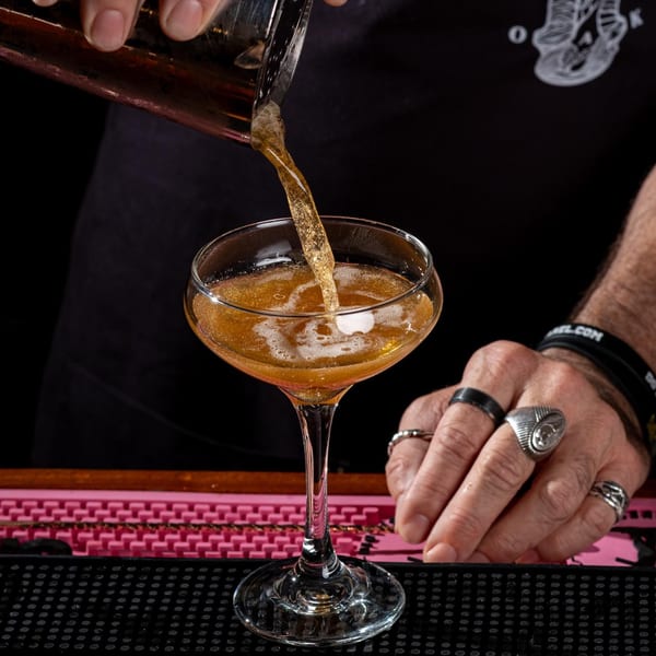 A bartender pours a golden cocktail from a shaker into a coupe glass at Black Oak on Fifth.