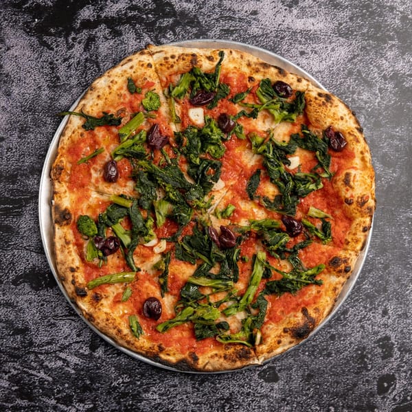 Black Oak on Fifth's Italian pizza with tomato sauce, green vegetables, and olives on a dark surface.