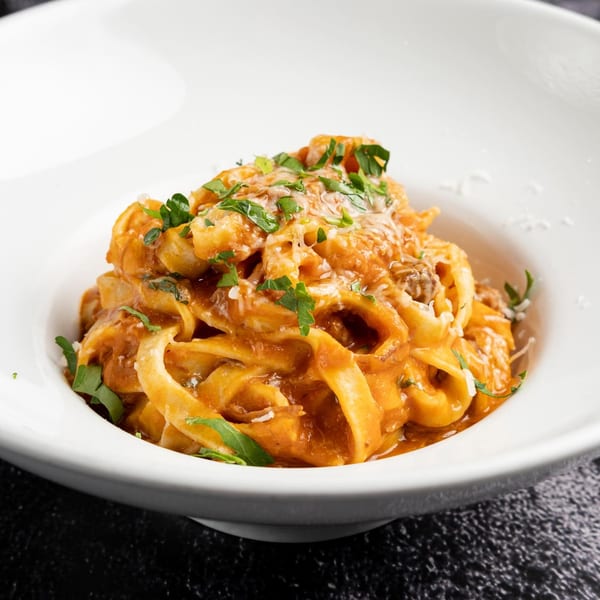 Fettuccine pasta with a creamy red sauce, garnished with fresh parsley and grated cheese.