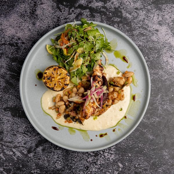 Grilled octopus with white beans, arugula salad, and a charred lemon on a light blue plate.