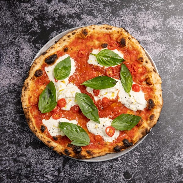 Neapolitan pizza with tomato sauce, fresh mozzarella, basil leaves, and cherry tomatoes on a dark surface.